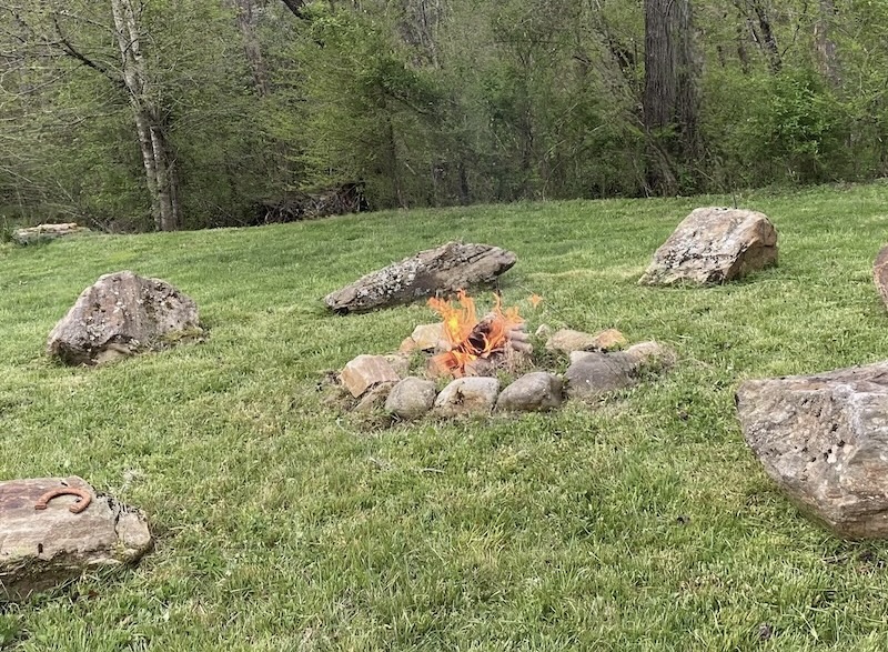 Stone fire ring with active fire surrounded by boulder seating in a spring meadow in Western North Carolina